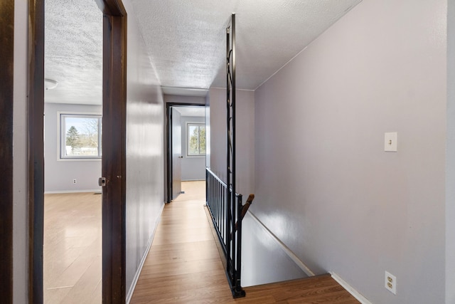 hall with light wood-type flooring, an upstairs landing, a textured ceiling, and baseboards