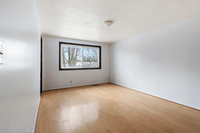 empty room featuring visible vents, baseboards, a textured ceiling, and light wood finished floors