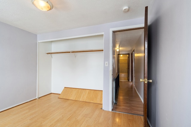 unfurnished bedroom with a closet, baseboards, a textured ceiling, and wood finished floors