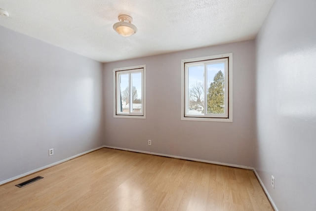 empty room with visible vents, plenty of natural light, a textured ceiling, and light wood finished floors