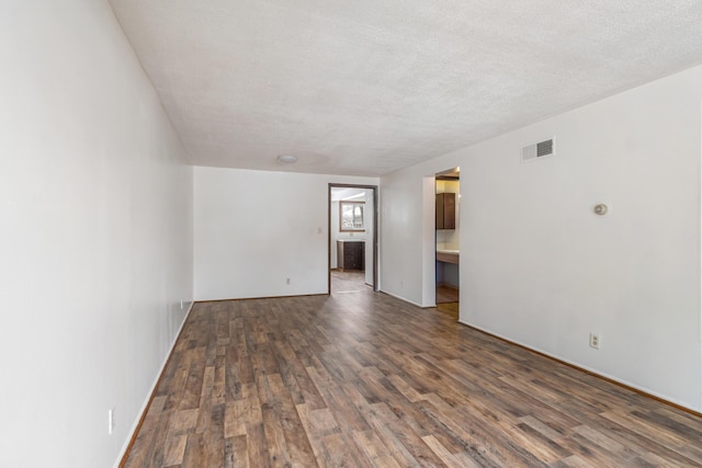 empty room with dark wood-style floors, visible vents, and a textured ceiling