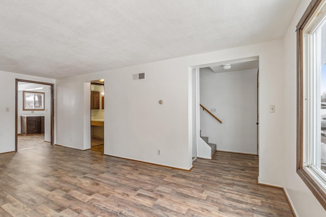 empty room featuring visible vents, a textured ceiling, stairs, and wood finished floors