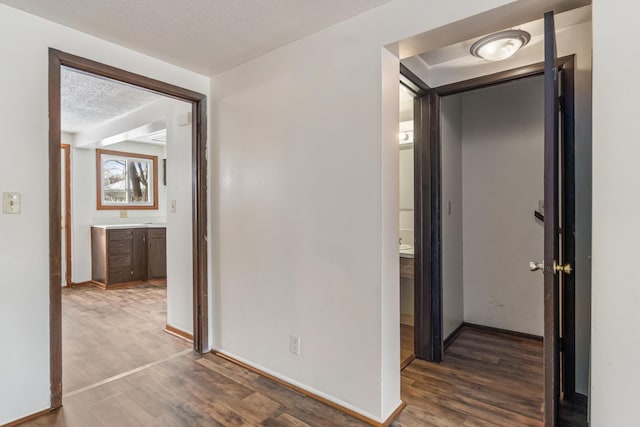 hall with wood finished floors, baseboards, and a textured ceiling