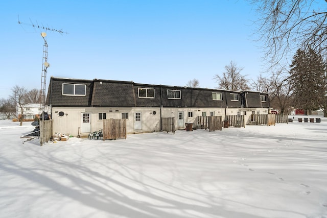 snow covered rear of property with mansard roof and fence