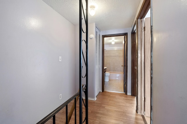 hall with baseboards, light wood finished floors, and a textured ceiling