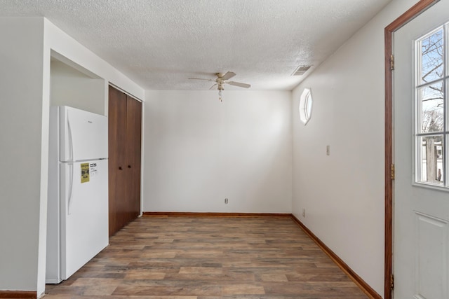 spare room with wood finished floors, a ceiling fan, visible vents, and a healthy amount of sunlight