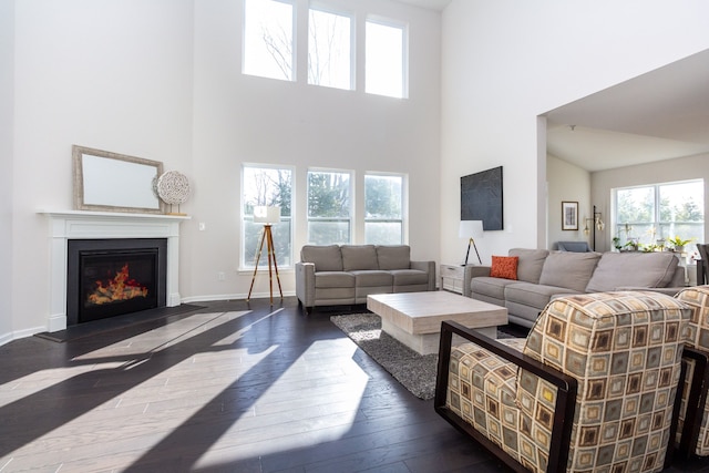 living room featuring hardwood / wood-style floors, a glass covered fireplace, baseboards, and a towering ceiling