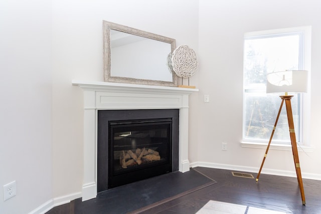 room details with a fireplace with flush hearth, visible vents, baseboards, and wood finished floors