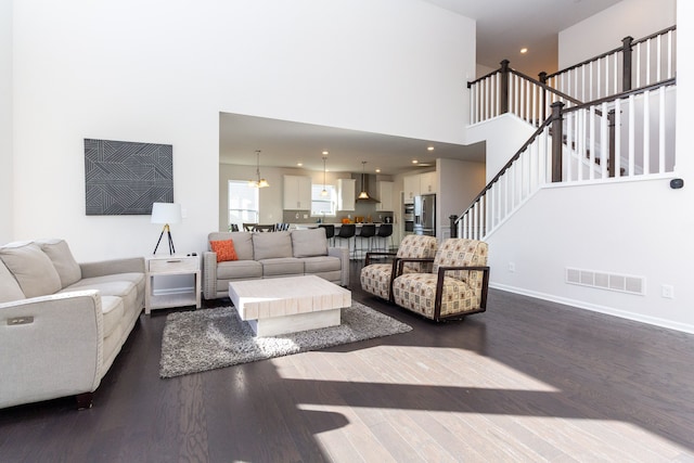 living area featuring dark wood finished floors, stairs, visible vents, and a towering ceiling