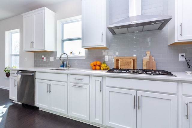 kitchen with a sink, dark wood-type flooring, light countertops, appliances with stainless steel finishes, and wall chimney range hood