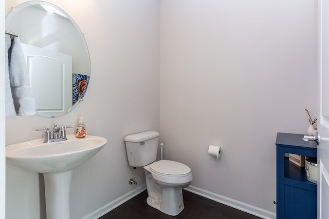 half bathroom featuring a sink, baseboards, toilet, and wood finished floors