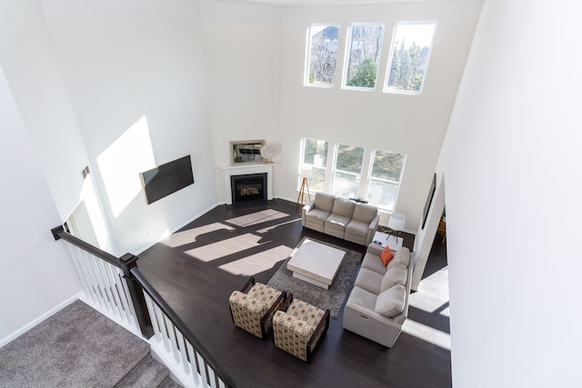 living area with wood finished floors, baseboards, visible vents, a fireplace, and a towering ceiling