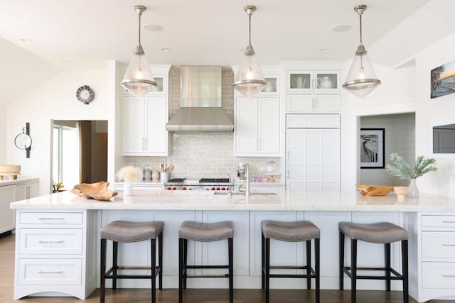 kitchen with a sink, backsplash, white cabinets, wall chimney range hood, and stove