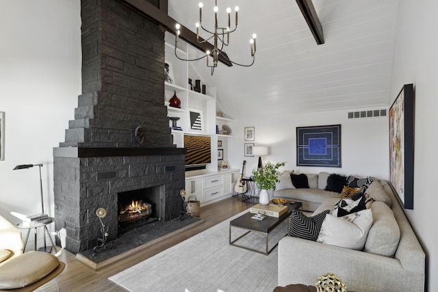 living area with visible vents, beamed ceiling, wood finished floors, a stone fireplace, and an inviting chandelier