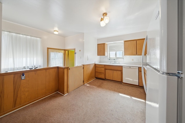 kitchen featuring white appliances, wooden walls, light countertops, light colored carpet, and brown cabinets