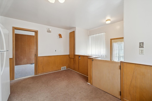 carpeted empty room featuring visible vents, wood walls, and wainscoting