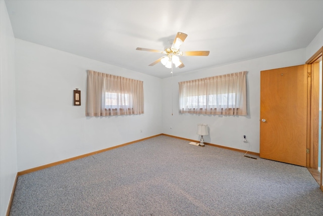 carpeted empty room with visible vents, baseboards, and a ceiling fan