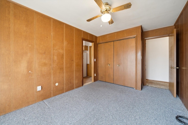 unfurnished bedroom featuring a closet, carpet flooring, wood walls, and a ceiling fan