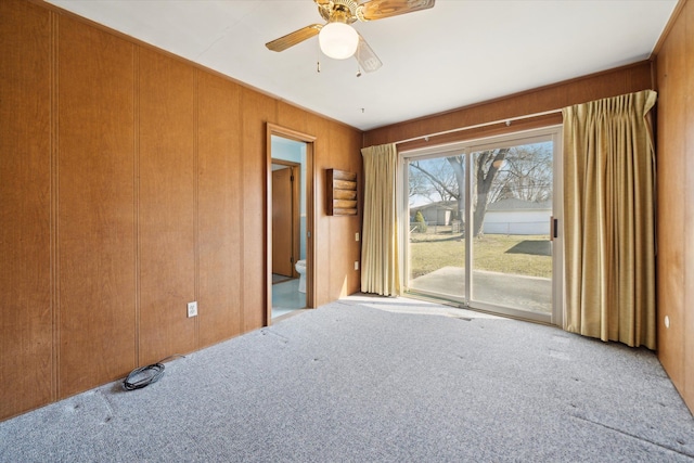 carpeted spare room featuring wooden walls and a ceiling fan