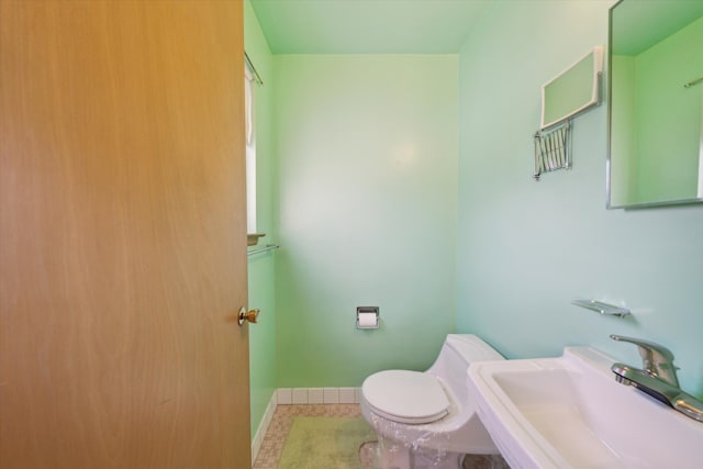 half bath with a sink, baseboards, toilet, and tile patterned flooring