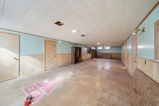 finished basement featuring wooden walls, a wainscoted wall, visible vents, and ornamental molding