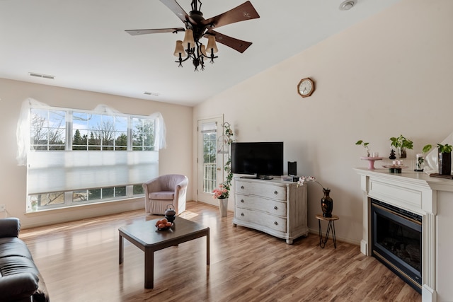 living room with visible vents, wood finished floors, a glass covered fireplace, and vaulted ceiling