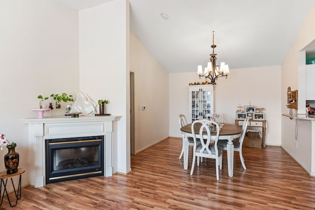 dining area with a glass covered fireplace, an inviting chandelier, wood finished floors, and vaulted ceiling