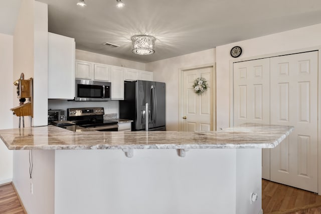 kitchen featuring light stone counters, appliances with stainless steel finishes, a breakfast bar, and a peninsula