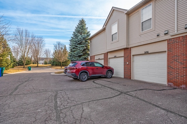 view of side of home featuring brick siding, an attached garage, and driveway