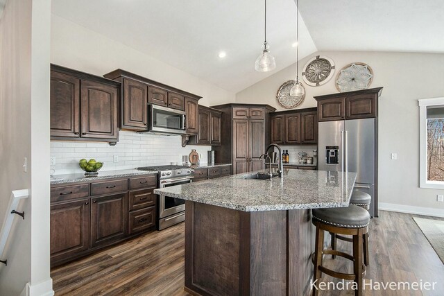 kitchen featuring dark brown cabinets, light stone countertops, dark wood-style floors, stainless steel appliances, and a sink