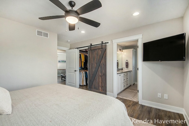 bedroom with wood finished floors, visible vents, baseboards, a spacious closet, and a barn door