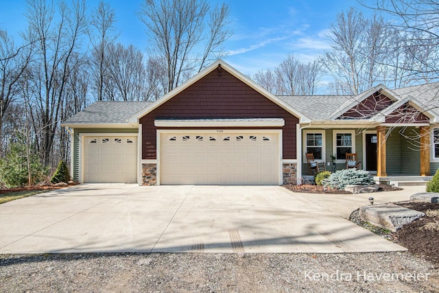 view of front of property with an attached garage, covered porch, a shingled roof, concrete driveway, and stone siding