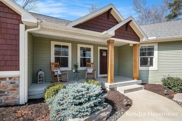 property entrance with stone siding, covered porch, and a shingled roof