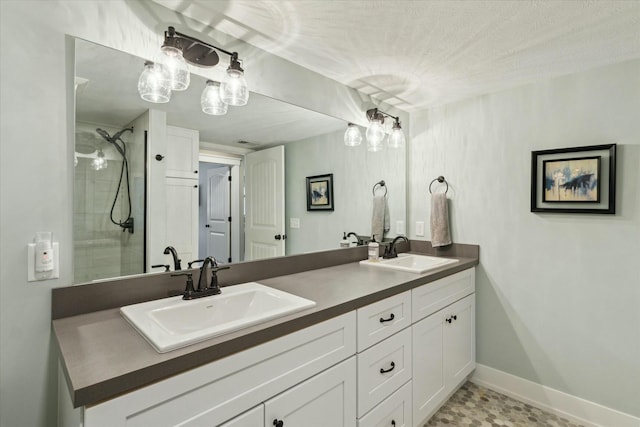 full bathroom with double vanity, tiled shower, baseboards, and a sink