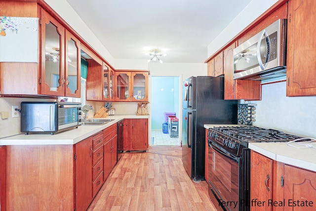 kitchen with light wood finished floors, black appliances, a sink, light countertops, and glass insert cabinets