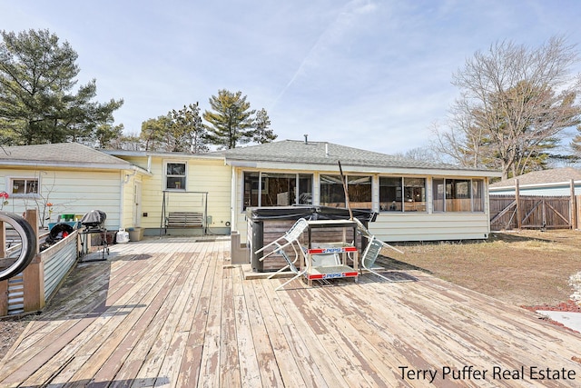 deck with a hot tub, fence, and a sunroom