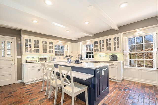 kitchen featuring a breakfast bar area, beam ceiling, brick floor, and a center island