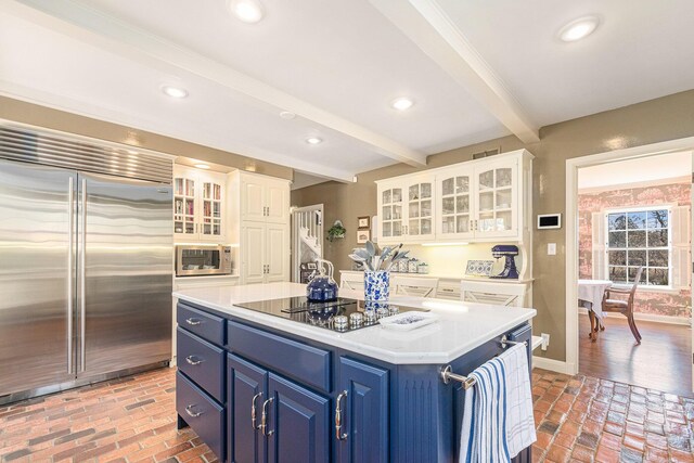 kitchen with white cabinets, appliances with stainless steel finishes, brick floor, blue cabinetry, and beamed ceiling
