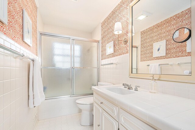 full bath featuring vanity, toilet, tile walls, tile patterned floors, and combined bath / shower with glass door