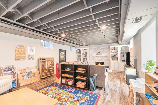 basement with visible vents, a large fireplace, and light wood finished floors