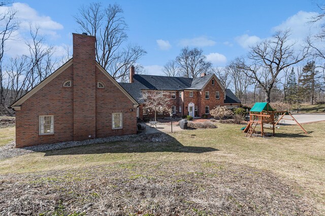 back of house featuring a playground, a chimney, a lawn, and brick siding