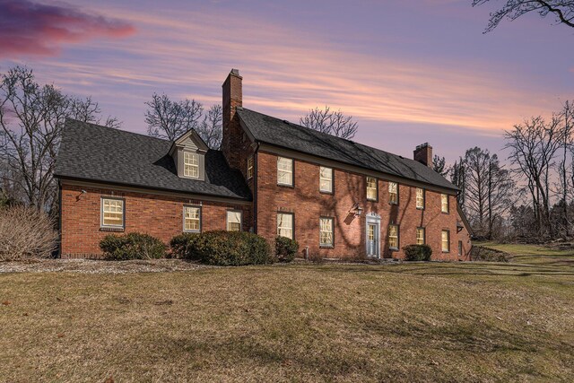 view of front of house with brick siding, a shingled roof, a front yard, and a chimney