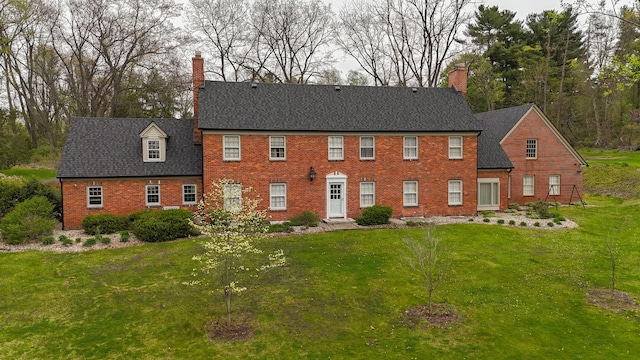 colonial home featuring roof with shingles, a chimney, a front yard, and brick siding