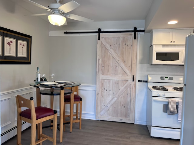 kitchen featuring a barn door, white appliances, dark wood-style flooring, and wainscoting