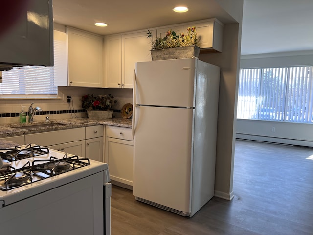 kitchen with baseboard heating, wood finished floors, white cabinets, white appliances, and a sink