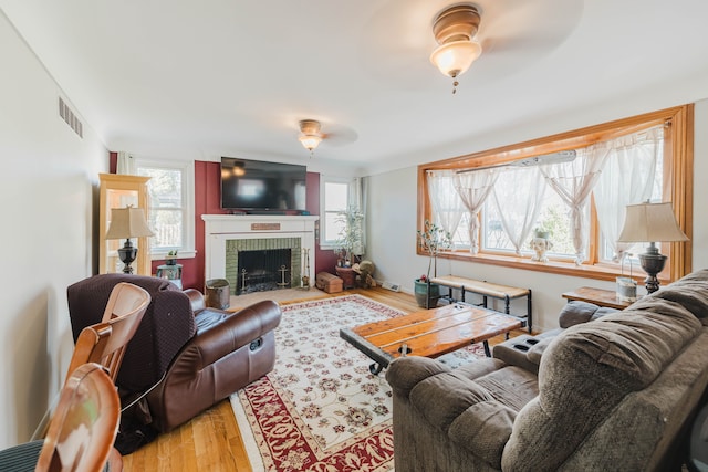 living room with visible vents, a healthy amount of sunlight, a brick fireplace, and wood finished floors