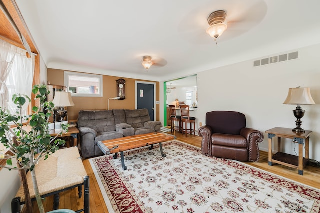 living room with visible vents, wood finished floors, and a ceiling fan