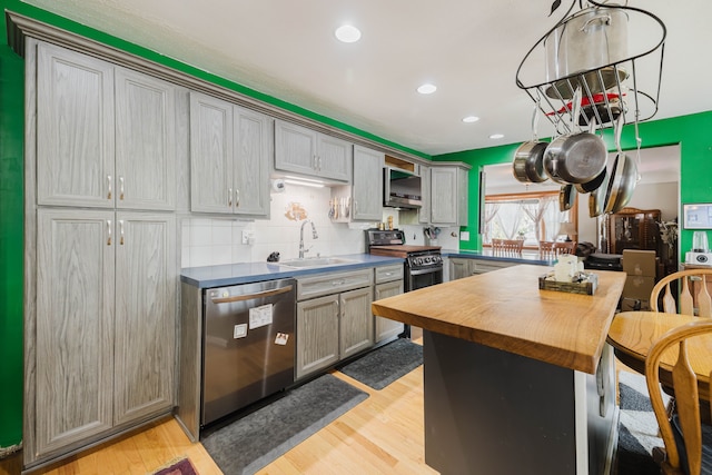 kitchen featuring a sink, stainless steel appliances, light wood-style floors, wood counters, and backsplash