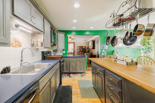 kitchen featuring electric range, light wood-style flooring, a sink, dishwasher, and tasteful backsplash