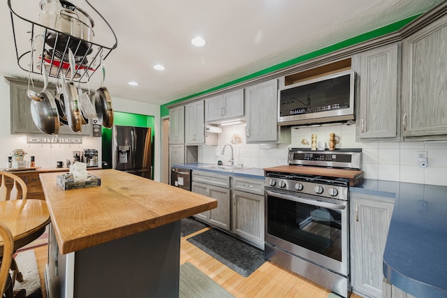 kitchen featuring light wood-style flooring, a sink, decorative backsplash, stainless steel appliances, and butcher block counters